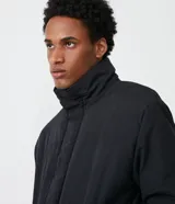 Campera puffer negra para hombre, con cuello alto, cierre frontal con botones a presión, bolsillos laterales y corte holgado. Fabricada en poliéster y poliamida.