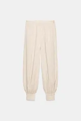 Pantalón bombacho de tiro medio, color beige claro, confeccionado en mezcla de lino. Presenta bolsillos laterales y bajo abullonado terminado en puño con botón.