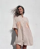 Camisola beige a rayas verticales blancas, con cuello mao, mangas cortas y dos bolsillos de gamuza en el pecho. Cierre frontal con botones.