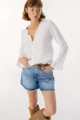 Blusa blanca de lino con botones de nácar, volados en el escote y mangas largas con puños acampanados. Corte recto y holgado.
