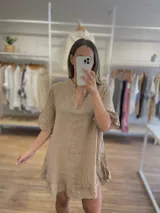 Vestido corto de lino color beige, con cuello en V y detalle de volado en el ruedo. Presenta mangas cortas abullonadas.