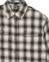 Camisa de franela a cuadros en tonos beige, gris y negro. Tiene cuello clásico, cierre con botones, dos bolsillos con solapa en el pecho y puños abotonados.