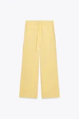 Pantalón de mujer color amarillo pálido, de corte ancho y tejido fluido. Tiene tiro medio, cintura elástica ajustable con cordones, bolsillos laterales y falsos bolsillos de vivo en la espalda.