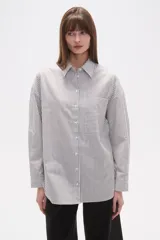 Camisa de algodón blanca de corte holgado, con cuello camisa y manga larga. Presenta un estampado de finas rayas verticales negras y un bolsillo frontal con rayas horizontales.