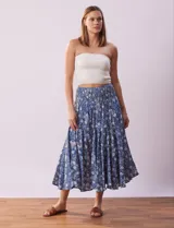 Falda midi de algodón estampada con flores blancas sobre fondo azul. Tiene pretina ancha elastizada en punto smock, ruedo con volados y forro interno a tono.