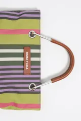 Bolso de mano mini de la marca Bimba y Lola con diseño de rayas verticales en tonos verde, violeta, rosado y blanco. Presenta estructura rígida, asas de mano de piel marrón con herrajes metálicos y una correa larga regulable. Incluye etiqueta frontal con el logo de la marca y cierre magnético.