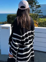 Sacón negro con rayas horizontales blancas, tejido tipo mohair, corte oversize y cinturón ajustable.
