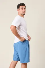 Bermuda deportiva de nylon color verde oliva, de corte suelto, con cintura elástica y cordón de ajuste. Cuenta con detalles de líneas verticales en los costados y bolsillos laterales con cierre.