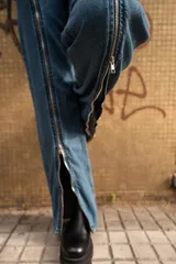 Pantalón de jean azul con cierre metálico en la parte inferior de la pierna.