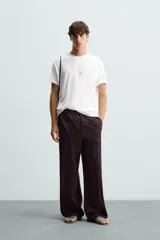 Camiseta blanca de corte holgado, cuello redondo y manga corta. Estampado frontal con texto en color negro y parche en la espalda. Detalle de pliegues en la espalda.