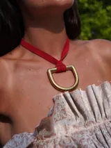 Collar con tira de cuero color suela y dije metálico dorado en forma de estribo.