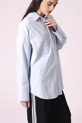 Camisa celeste de corte amplio, con cuello clásico, cierre frontal con botones y bolsillo en el pecho.