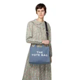 Bolso tote negro de lona con asas de mano y correa bandolera ajustable. Estampado frontal con la leyenda "THE TOTE BAG MARC JACOBS" en letras blancas.