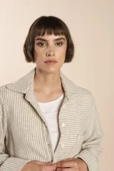 Camisa larga color crema con rayas verticales finas en gris, con botones dorados y bolsillo plaque en la delantera.