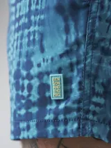 Short de baño color borgoña con estampado de hojas en tono sobre tono, cintura elástica con cordón ajustable y logo de la marca en la pierna.