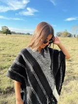 Ruana tejida a mano en telar, confeccionada en lana Merino color negro con detalles en blanco y flecos blancos.