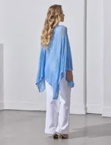 Poncho blanco de tejido calado con lurex, terminación asimétrica y cuello redondo.