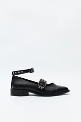 Zapato tipo zueco negro de cuero sintético con punta fina, taco bajo y correa al tobillo con hebilla metálica.