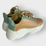 Zapatillas urbanas color mostaza, con detalles en verde menta y naranja. Confeccionadas en cuero sintético con cordones beige y suela de plataforma blanca.