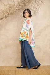 Camisa de manga corta con cuello clásico y cierre frontal con botones. Presenta un estampado con motivos florales, frutales y paisajes.