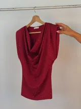 Blusa color borgoña con cuello drapeado, mangas cortas con hombreras y pequeños lunares plateados.