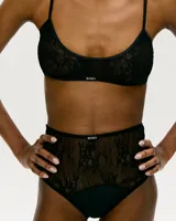 Conjunto de lencería negro de encaje, compuesto por un corpiño triangular de breteles finos y una bombacha de tiro alto con paneles de encaje transparente.