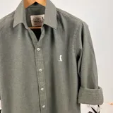 Camisa de vestir verde musgo, de corte clásico, con cuello italiano, manga larga con puños abotonados y logo bordado en el pecho.