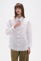 Camisa de algodón blanca, de corte ancho, con botones de madera y detalles de encaje calado en el frente, mangas y ruedo. Tiene cuello camisero y manga larga.