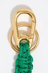 Llavero con mosquetón metálico dorado, cordón trenzado azul con motas blancas y dije en forma de corazón naranja con centro dorado y el nombre de la marca grabado.