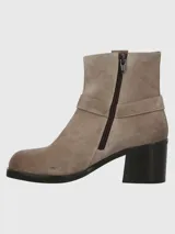Bota corta de cuero color taupe, con caña de 14 cm, taco cuadrado de 6 cm y punta cuadrada. Presenta una correa con hebilla metálica alrededor del tobillo y cierre lateral.