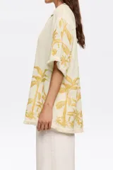 Camisa color crema con bordado de hojas color mostaza, de corte recto, manga corta y cuello camisero.