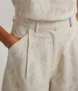 Bermuda corta color beige con estampado floral bordado, de corte sastrero, con bolsillos frontales, cierre por cremallera y botón de presión.