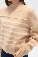 Sweater beige con rayas horizontales negras, cuello alto y corte holgado.