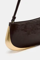 Bolso de hombro alargado color marrón oscuro, con asa corta y detalle metálico dorado en un lateral. Incluye bolsillo interior con cremallera y cierre principal con cremallera.