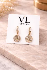 Aretes colgantes dorados con aro pequeño cubierto de micro strass. El dije es circular, con un diseño de estrella central rodeada de cristales, simulando una brújula o estrella náutica.