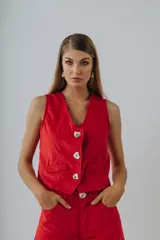 Chaleco rojo de pana con botones blancos en forma de corazón, cuello en V y bolsillos frontales simulados.