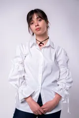 Camisa blanca de mangas largas abullonadas con lazos en los puños y cuello clásico. Cierre frontal con botones.