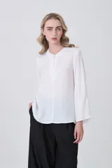 Blusa blanca de poliéster, entallada, con escote en V y botones frontales. Presenta mangas largas con puños anchos.