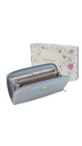 Billetera larga color mostaza con textura rugosa, cierre perimetral con deslizador metálico y placa rectangular con logo en el frente.