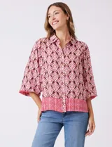 Camisa de gasa con cuello con solapa y apertura central con botones. Presenta un estampado de patrones geométricos en tonos rosados, marrones y crema, con un borde inferior en un patrón geométrico más denso en tonos rojizos/rosados. Las mangas son amplias de largo tres cuartos con puño elastizado.