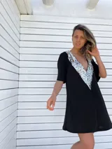 Túnica corta negra con escote en V profundo y apliques de lentejuelas plateadas en el borde del escote.