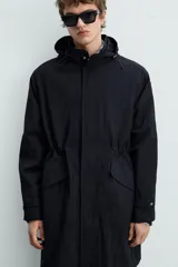 Parka negra de tejido técnico ligero, corte regular, cuello alto con capucha ajustable, manga larga con puños ajustables, cintura ajustable con cordón interno, bolsillos de solapa en la cadera, abertura en la espalda y cierre frontal con cremallera oculta y botones a presión.