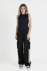 Pantalón negro de corte ancho con cintura elastizada y cordón ajustable. Presenta una franja vertical blanca a lo largo de la pierna y un bolsillo tipo cargo en el muslo.