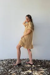 Vestido corto color beige de voile de rayon, con cuello bebé con volados y mangas cortas abullonadas.