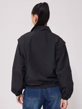 Campera negra tipo rompevientos de nylon con cierre frontal y bolsillos laterales.