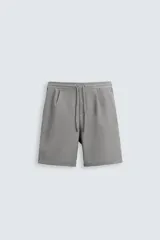 Bermuda gris de cintura elástica ajustable con cordón, detalle de pliegues frontales, bolsillos delanteros y traseros.