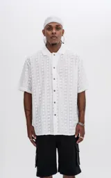 Camisa blanca con textura y botones marrones, de corte holgado y mangas cortas.