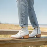 Botines de cuero vacuno color blanco con diseño bordado, taco de madera foliado en cuero de 5cm, cierre del lado interior y horma de punta fina.