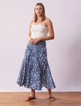 Falda midi de algodón estampada con flores blancas sobre fondo azul. Tiene pretina ancha elastizada en punto smock, ruedo con volados y forro interno a tono.