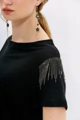 Remera blanca de lino con mangas cortas y calce al cuerpo. Presenta cadenas de strass en los hombros.